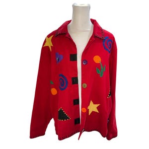 May include: A bright red long-sleeve jacket featuring a collar and a front button closure with multicolored buttons. The jacket is decorated with various fabric appliqués including yellow stars, blue spirals, a purple heart, and a green-stemmed orange flower.