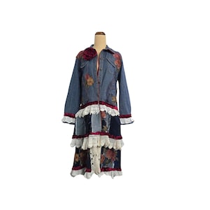 May include: A long denim jacket with floral embroidery and patchwork detailing. The jacket features a tiered skirt with lace and velvet trim. A large red flower is pinned on the shoulder. The jacket is displayed on a mannequin.