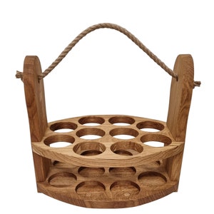 May include: A wooden bottle carrier with a rope handle. The carrier has two tiers with 12 circular cutouts for holding bottles. The carrier is made of natural wood with a light brown finish.