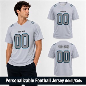 May include: A light gray V-neck football jersey featuring the text YOUR TEAM and the number 00 on the front, with the text YOUR NAME and the number 00 on the back. The design includes dark gray and teal accents on the shoulders and numbers.