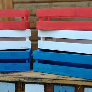 May include: Three wooden crates stacked on top of each other. The top crate is red, the middle crate is white, and the bottom crate is blue.