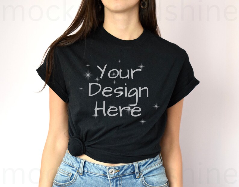 May include: A black t-shirt with the text "Your Design Here" in white lettering and small white stars. The shirt is worn by a person with long brown hair and is knotted at the waist.