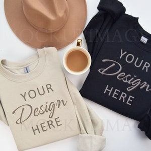 May include: Two sweatshirts, one beige and one black, laid flat on a white surface. Both sweatshirts have the text "YOUR Design HERE" printed on the front. A brown hat and a cup of coffee are also in the image.