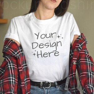 Könnte beinhalten: Ein weißes T-Shirt mit dem Text "Your Design Here" in schwarzer Handschrift. Das Shirt wird von einer Person mit einem rot-schwarzen karierten Hemd darüber getragen.