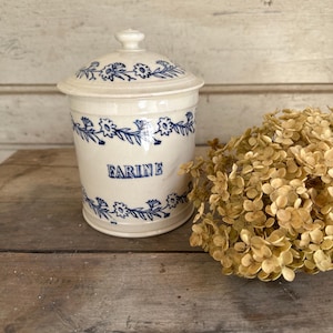 Può includere: Un contenitore in ceramica color crema con coperchio abbinato, caratterizzato da motivi a tralci floreali blu sulla parte superiore e inferiore. La parola FARINE è stampata in lettere blu sulla parte anteriore del contenitore cilindrico.