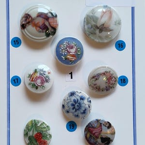 Può includere: Una collezione di sette bottoni rotondi in porcellana numerati 1, 15, 16, 17, 18, 19, 20 e 21. I bottoni presentano vari disegni dipinti a mano, inclusi motivi floreali, frutta e figure. La scheda di presentazione riporta il testo BOUTONS de Limoges.