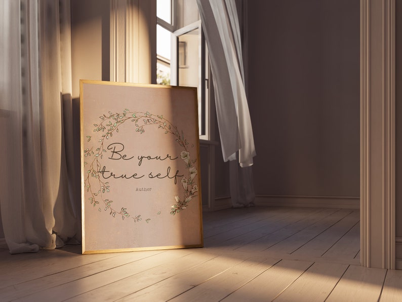 May include: A framed print with a floral wreath and the text "Be your true self" with the author "Aulthor" below. The print is on a light brown background and has a gold frame. The print is sitting on a wooden floor.