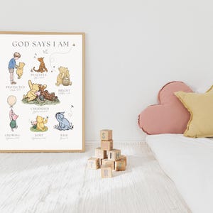 Puede incluir: Un p&oacute;ster enmarcado con el texto "GOD SAYS I AM" e ilustraciones de personajes de Winnie the Pooh. El p&oacute;ster presenta varios personajes con palabras como "Protegido" y "Amable". Una pila de bloques de madera y cojines decorativos est&aacute;n en primer plano.