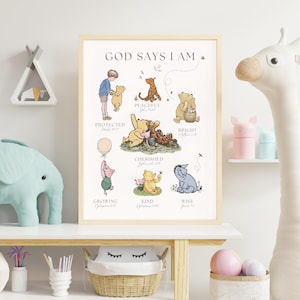 Puede incluir: Un estampado enmarcado con personajes de Winnie the Pooh y el texto "GOD SAYS I AM". Las ilustraciones muestran a Pooh y sus amigos con palabras como "Protegido", "Pac&iacute;fico" y "Atesorado". La obra de arte est&aacute; en un marco de madera clara.