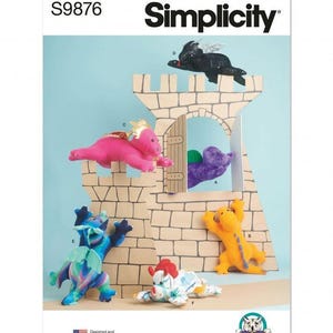 May include: A Simplicity S9876 sewing pattern envelope featuring a cardboard castle structure with six plush dragon toys in various colours including black, pink, purple, blue, orange, and white with red accents, designed and printed in the USA.