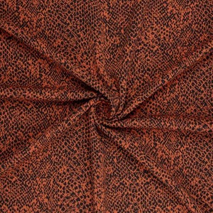 Op de afbeelding: Een stof met een herhalend zwart slangenpatroon gedrukt op een effen, gebrand oranje achtergrond. Het materiaal is in het midden samengebracht, waardoor natuurlijke plooien en draperingen ontstaan die de textuur en de print benadrukken.