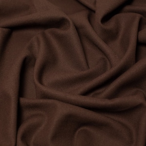 May include: Close-up of a brown fabric with a soft, textured surface. The fabric is folded and draped, creating a smooth, flowing look.