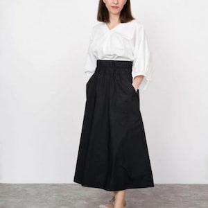 May include: A woman wearing a white blouse and a black skirt with a high waist. She is wearing white sandals with a platform.