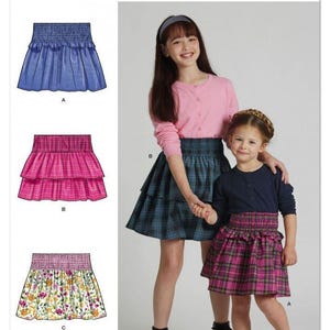 Puede incluir: Patrón de costura Simplicity S3175 con ilustraciones de tres variantes de falda: una falda azul con volantes, una falda rosa de cuadros con niveles y una falda con estampado floral. El sobre muestra a dos modelos con estas faldas.