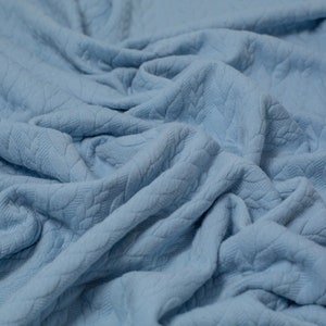 May include: A soft, blue, textured fabric with a subtle pattern. The fabric is folded and draped, showing its texture and drape.