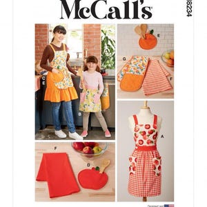 May include: McCall's M8234 sewing pattern envelope featuring illustrations of kitchen textiles including aprons with apple and citrus prints, a red apple-shaped pot holder, a double oven mitt, and a red kitchen towel, all labelled with letters A through G.
