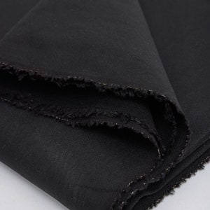 May include: Black fabric with a slightly textured surface. The fabric is folded and has a silver thread running along the edge.