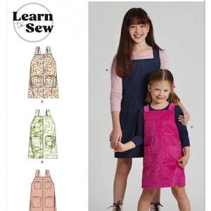May include: Simplicity sewing pattern S3174 Learn to Sew features three variations of a sleeveless pinafore dress with two front pockets. The pattern displays a floral print, a light green patterned design, and a solid pink corduroy fabric option.