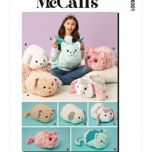 Op de afbeelding: McCall's M8301 naaipatroon met vijf pluche dierontwerpen gelabeld van A tot E. De collectie bevat een beige kat, een witte hond, een grijs-witte konijn, een roze kat en een lichtblauwe draak met vleugels en een staart.