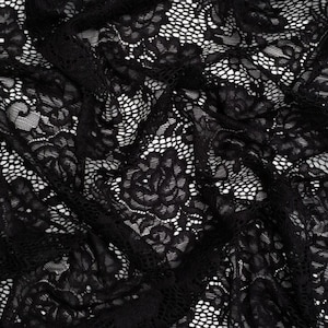 Puede incluir: Una tela de encaje negro con un patrón floral detallado de rosas sobre un fondo de malla intrincado. El material está plegado para crear profundidad y textura, resaltando la calidad delicada y semitransparente del bordado floral en toda la pieza.