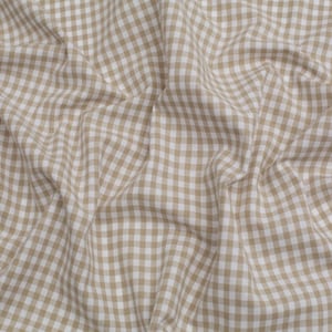 Op de afbeelding: Een bruine en witte gingham stof met een geruit patroon. De stof is gekreukt en heeft een zachte textuur.