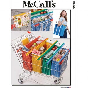 Op de afbeelding: McCall's M8420 naaipatroon-envelop met instructies voor meerkleurige herbruikbare boodschappentassen die in een metalen winkelwagentje kunnen worden gehangen. Het patroon bevat verschillende tasstijlen gelabeld A, B, C, F en G, getoond in rode, gele, groene en blauwe stoffen, waarbij één versie een zonnebloemenprint heeft.