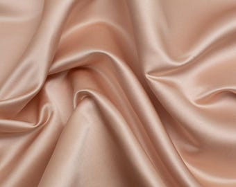 Puede incluir: Una pieza de tela de satén color rosa rubor con una superficie lisa y lustrosa con un brillo reflectante. El material está drapeado en pliegues suaves y fluidos que crean sombras y luces profundas, enfatizando la textura fluida del tejido.