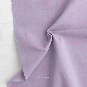 May include: A solid light purple fabric with a visible woven texture and a matte finish. The word FABLEISM is printed in small white capital letters near the bottom centre of the fabric, which is draped to show folds and depth in the material.