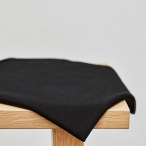Op de afbeelding: Een zwarte stofstaal gevouwen op een houten tafel. De stof is glad en heeft een lichte glans.