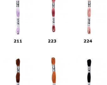 May include: D.M.C. Size 16 Coton A Broder Special embroidery thread in six colors: light purple 211, dusty rose 223, soft pink 224, dark brown 300, orange 301, and black 310. Each skein features a central paper label with the brand logo and color number.