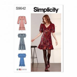 Puede incluir: Patrón de costura Simplicity S9642 que presenta un vestido con cuello en V, mangas abullonadas y dobladillo con volantes. El patrón incluye ilustraciones de tres variaciones de vestido en rosa, azul estampado y azul liso, junto a una foto.