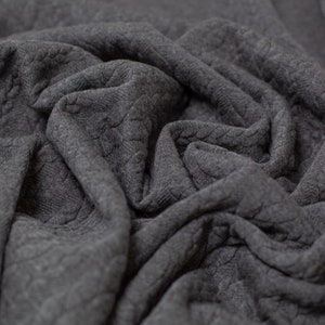 May include: Close-up of a gray knitted fabric with a textured cable knit pattern. The fabric is soft and has a slightly fuzzy texture.
