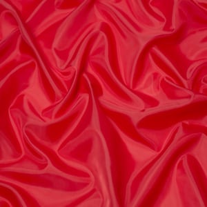 May include: A close-up of a smooth, red fabric with soft, flowing folds. The fabric has a subtle sheen and a luxurious feel.