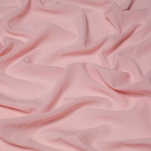 Pode incluir: Um tecido macio e rosa com uma textura lisa e rugas sutis. O tecido é drapeado e dobrado, criando um visual fluido e elegante.