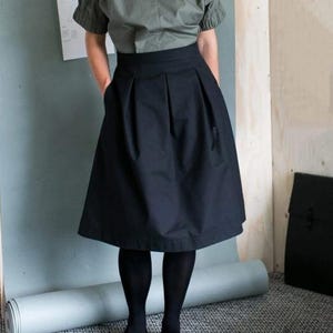 May include: A woman is wearing a black skirt with pleats and a green top. She is wearing black tights and blue heels.