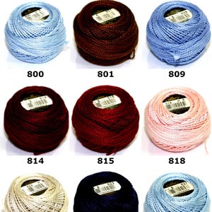 Pode incluir: Nove novelos de linha D.M.C. Cotton Perle tamanho 5 em várias cores, incluindo azul claro, castanho escuro, azul médio, vermelho escuro, bordeaux profundo, rosa claro, bege, azul marinho e azul celeste, cada um com o número da cor.