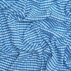 Könnte beinhalten: Ein Stoffstück mit einem klassischen blau-weißen Vichy-Karo-Muster. Das Material ist in weichen, fließenden Falten und Drapierungen angeordnet, wodurch eine strukturierte Oberfläche entsteht, die das sich wiederholende kleine quadratische Gittermuster betont.