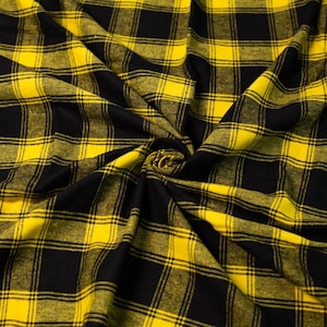 Puede incluir: Tela de cuadros amarillos y negros con textura tejida. La tela está doblada y dispuesta en un patrón de remolino.
