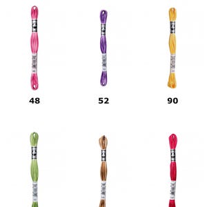 Puede incluir: Seis madejas de hilo para bordar D.M.C. Coton A Broder Special tamaño 25 dispuestas en dos filas. Los colores son rosa, morado, amarillo, verde claro, bronceado y rojo oscuro, etiquetados con los números 48, 52, 90, 92, 105 y 107.