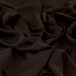 May include: Close-up of a dark brown fabric with a smooth, silky texture. The fabric is draped and folded, creating soft, flowing lines.