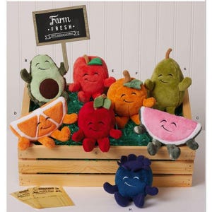 Peut inclure: Patron de couture Simplicity S3184 pour peluches en forme de fruits et légumes. L'image montre des personnages en peluche avocat, pomme, orange, poire et myrtille souriants dans une caisse en bois, avec un panneau Farm Fresh et des papiers.