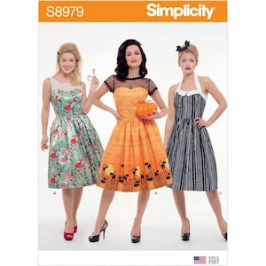 May include: Simplicity pattern S8979 featuring three knee-length dresses. The first is green with a colourful print, the second is orange with a black cat and moon print and black lace yoke, and the third is a black and white vertical striped dress.