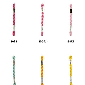 May include: Six skeins of D.M.C. Size 5 Cotton Perle Thread arranged in two rows. The colors include shades of pink labeled 961, 962, and 963, followed by light green 966, and yellow shades 972 and 973. Each skein features a branded paper label.