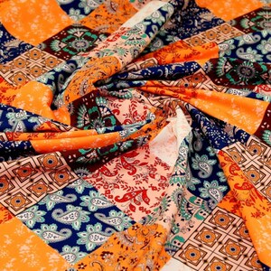 May include: A colourful fabric with a patchwork design featuring orange, blue, green, and brown paisley patterns. The fabric is made of a soft, lightweight material and has a smooth texture.