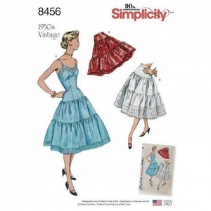 May include: Simplicity sewing pattern 8456 for 1950s vintage clothing. The envelope displays illustrations of a light blue dress with lace trim, a red patterned tiered skirt, and a white tiered skirt with lace trim, along with the text 90th anniversary.