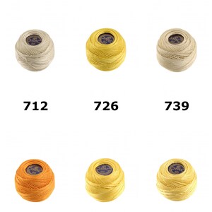 Peut inclure: Six pelotes de fil de coton 3 brins D.M.C. Fil a Dentelles disposées sur deux rangées. Les couleurs incluent crème, jaune vif, beige clair, orange, jaune doré et jaune pâle, étiquetées avec les numéros 712, 726, 739, 740, 743 et 744.