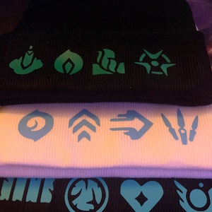 May include: Three black knit beanies with different colored designs. The top beanie has green designs, the middle beanie has white designs, and the bottom beanie has blue designs.