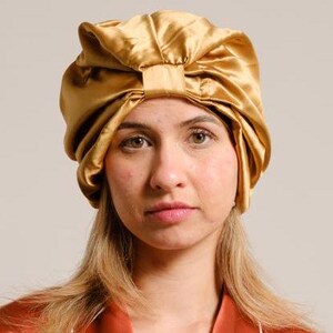 Pu&ograve; includere: Un copricapo da notte in raso dorato con un fiocco in cima. Il copricapo &egrave; indossato da una persona con capelli lunghi e biondi.