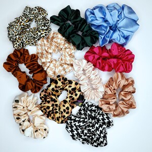 May include: A collection of 11 colourful hair scrunchies in various patterns and fabrics, including leopard print, floral, and solid colours.