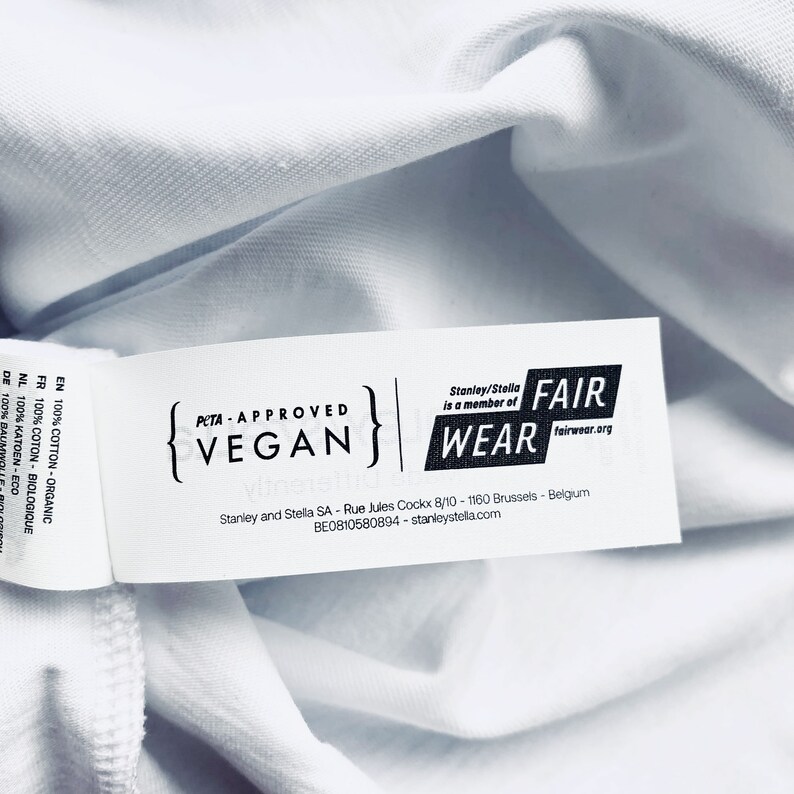 May include: White clothing label with black text that reads "PETA-APPROVED VEGAN" and "Stanley/Stella is a member of FAIR WEAR fairwear.org". The label also includes the company name, address, and website.